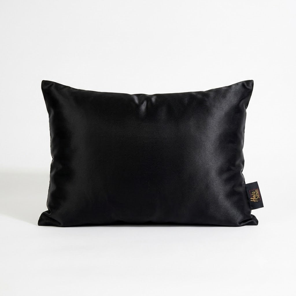A black satin rectangular pillow with a small black fabric tag on the right side, photographed against a clean white background.